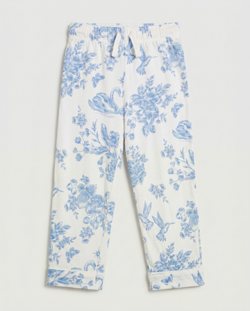 Full flat lay front view:
Girls' pyjama pants in ivory with an all-over blue toile de Jouy print featuring hummingbirds, swans, strawberries, and floral motifs, displayed flat lay on a white background with a relaxed straight leg and folded cuff hem.