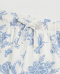 Close-up waistband detail:
Close-up of the elasticated waistband on girls' toile de Jouy pyjama pants, showing a woven ivory drawstring tied in a bow with blue floral and bird print fabric detail.