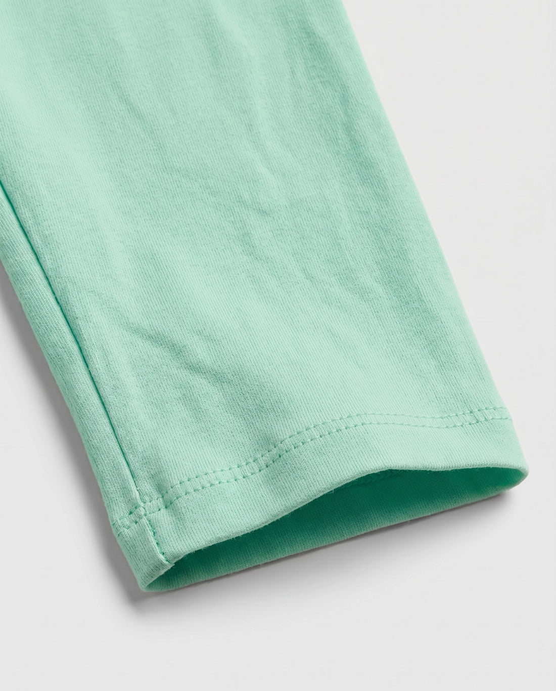 Full-length girls' slim-fit leggings in fresh mint green with a small rainbow and cloud "Miracle" graphic on the upper right hip, elasticated waistband, laid flat on a light grey background.