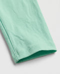 Close-up of girls' mint green cotton leggings showing clean double-stitched ankle hem detail and soft breathable fabric texture on a light grey background.