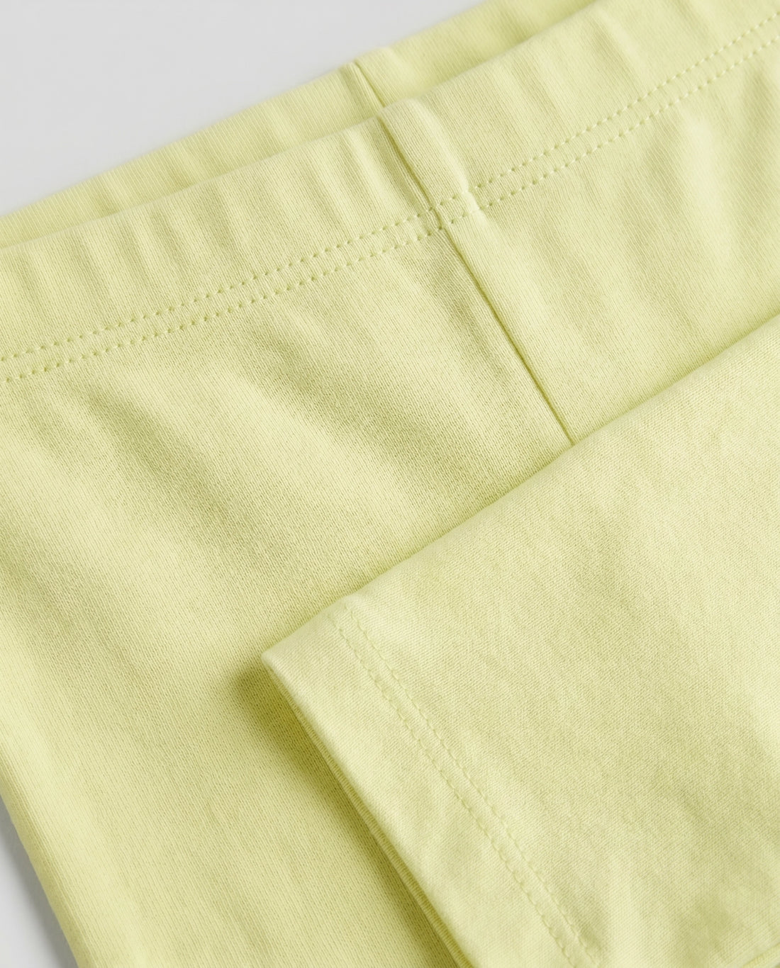 Close-up of girls' soft lime yellow cotton leggings showing elasticated waistband detail, quality stitching and smooth breathable fabric texture.