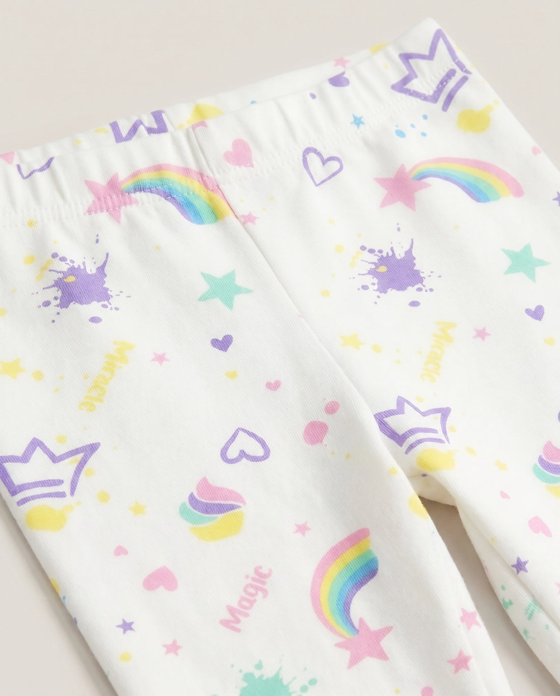 
Full-length white girls' slim-fit leggings with all-over pastel magic-themed print including rainbows, stars, hearts, crowns, cupcakes and paint splashes, laid flat on a white background.