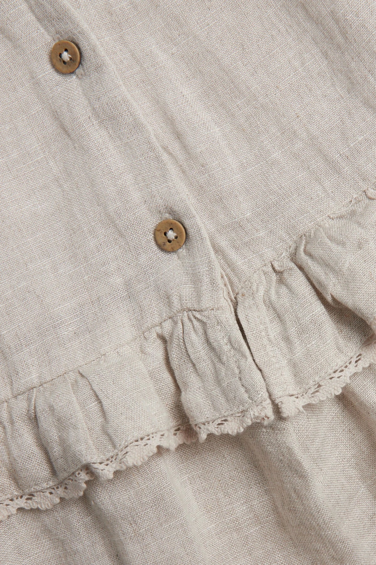 Close-up of girls’ beige linen dress fabric with wooden buttons and lace-trimmed ruffle detail