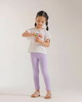 Young girl wearing baby purple full-length cotton leggings styled with a cream flutter-sleeve top and nude sandals, standing against a light grey background.