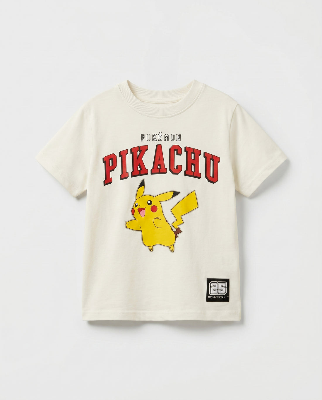 Flat lay of a boys' off-white short-sleeve t-shirt with Pikachu varsity arch print in red, full-body character graphic, and a small woven badge patch at the hem