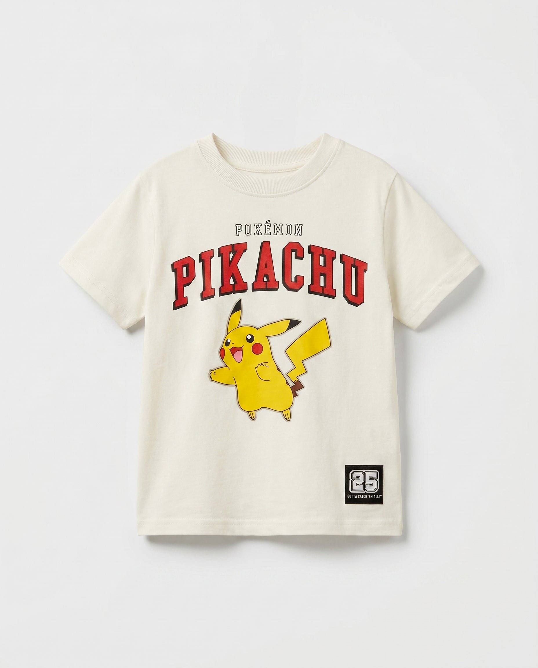 Flat lay of a boys' off-white short-sleeve t-shirt with Pikachu varsity arch print in red, full-body character graphic, and a small woven badge patch at the hem