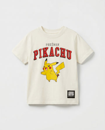 Flat lay of a boys' off-white short-sleeve t-shirt with Pikachu varsity arch print in red, full-body character graphic, and a small woven badge patch at the hem