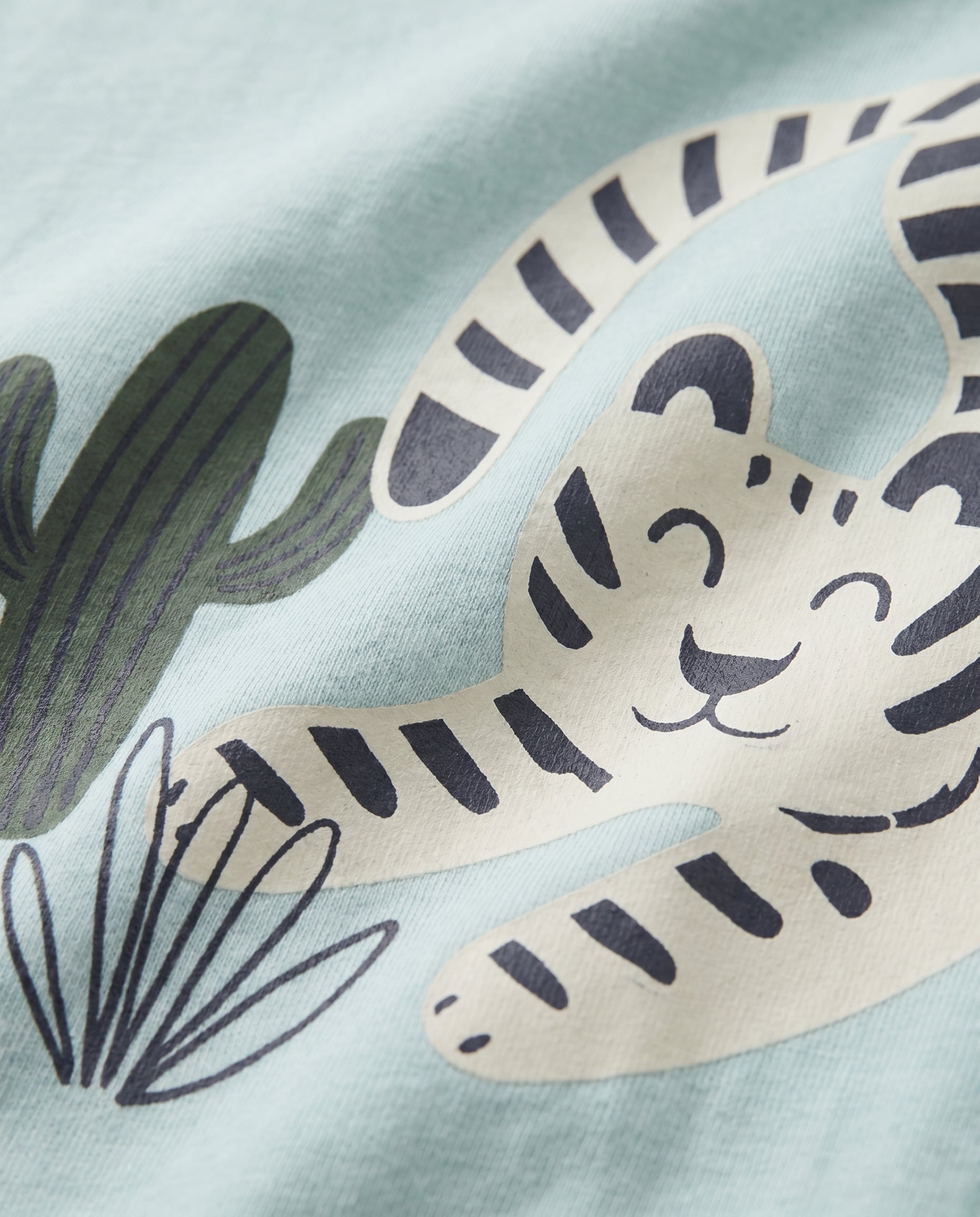 Close-up of striped big cat and cactus graphic print on mint blue boys' cotton t-shirt, showing cream and navy illustrated design detail