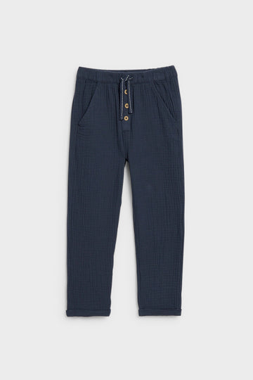Navy blue kids' muslin trousers with drawstring waist, button placket and side pockets, flat lay — PTex Fashion