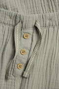 Close-up of coconut-look button placket and drawstring on sage green kids' muslin trousers — PTex Fashion