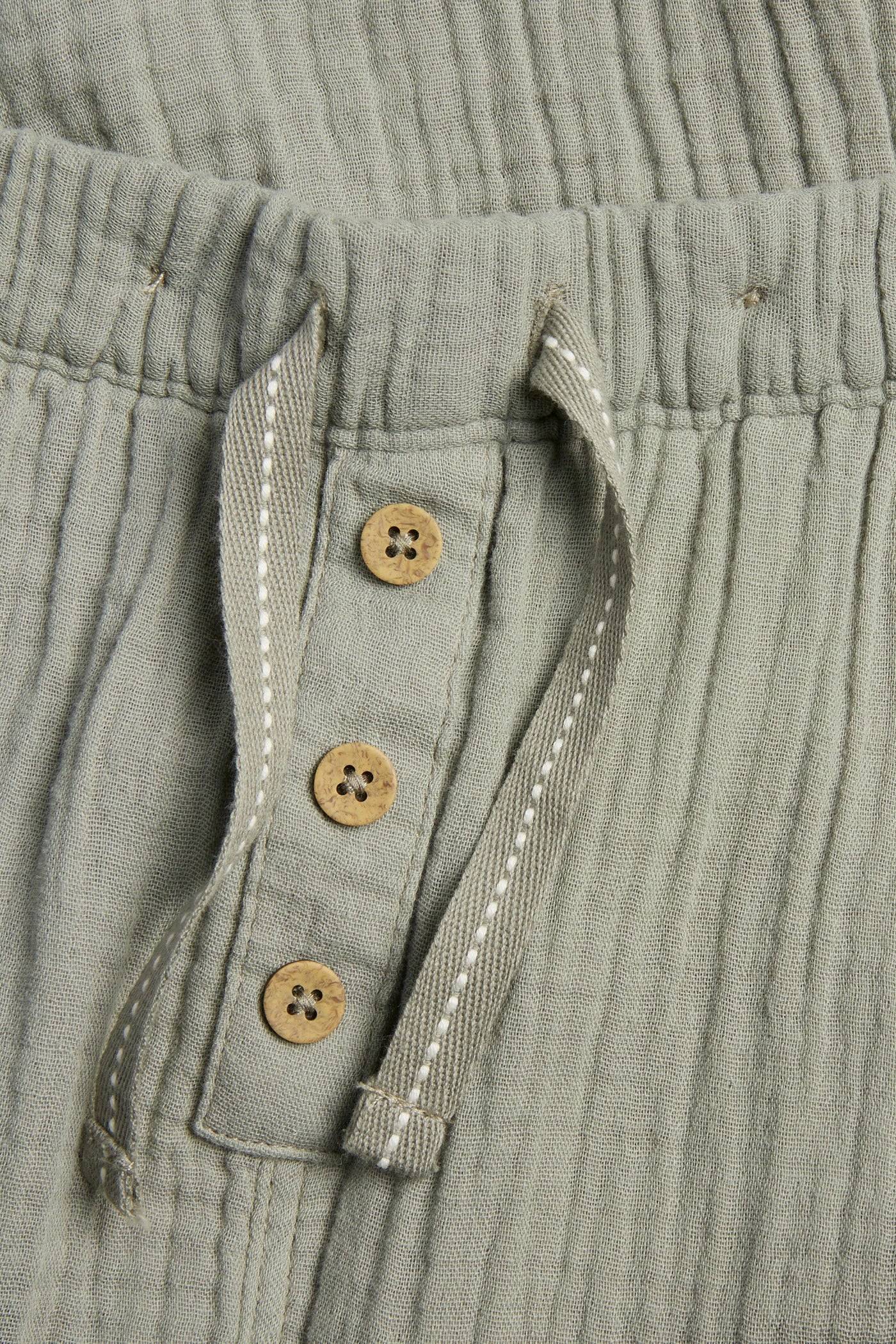 Close-up of coconut-look button placket and drawstring on sage green kids' muslin trousers — PTex Fashion