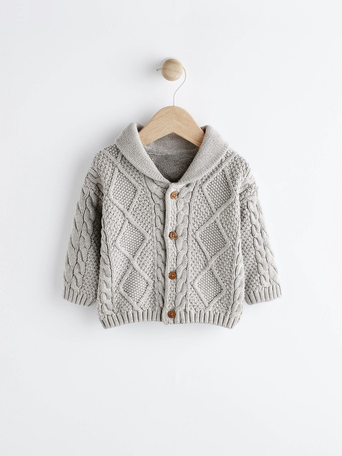 Knitted baby cardigan on a hanger against a white background