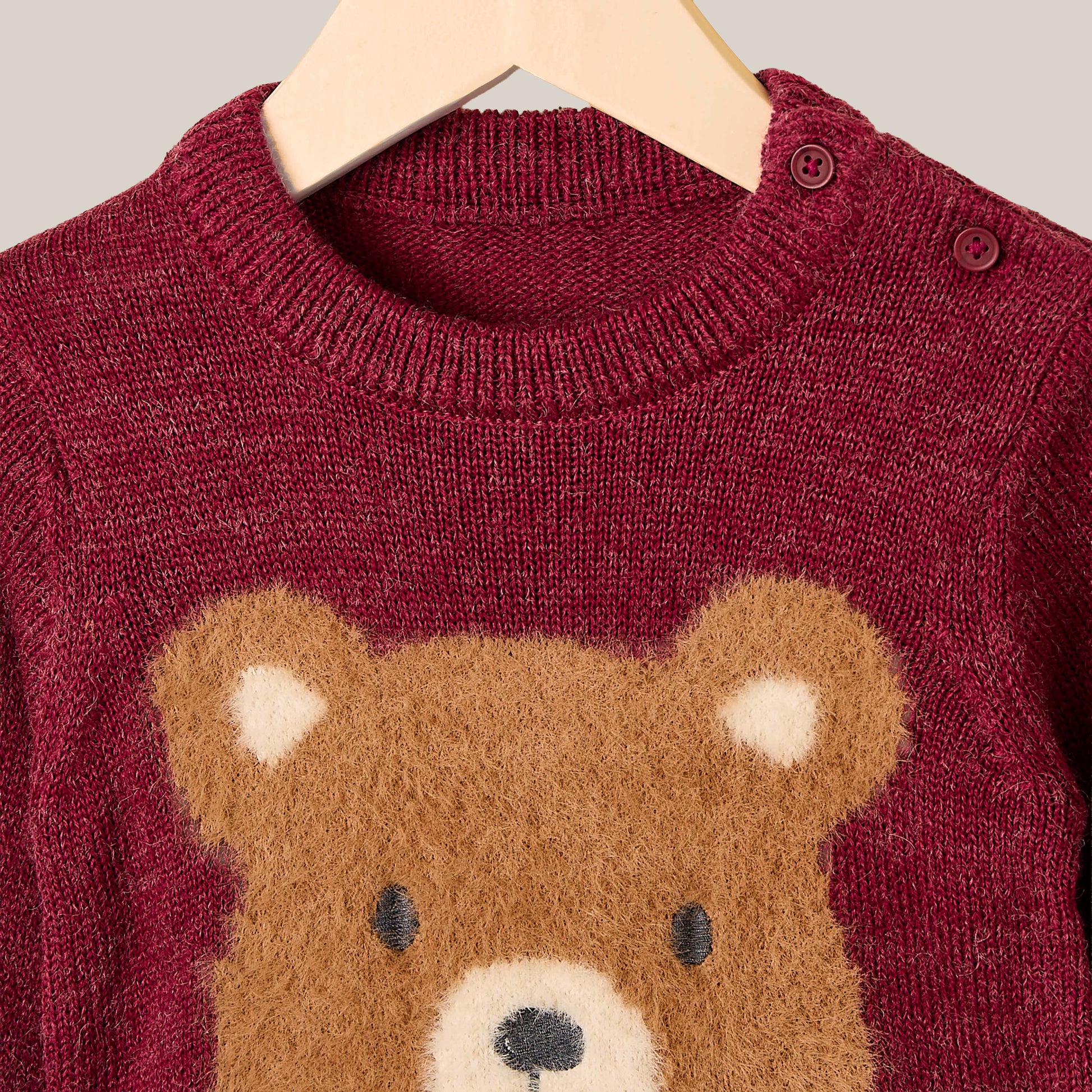 Maroon sweater with a teddy bear design on a hanger