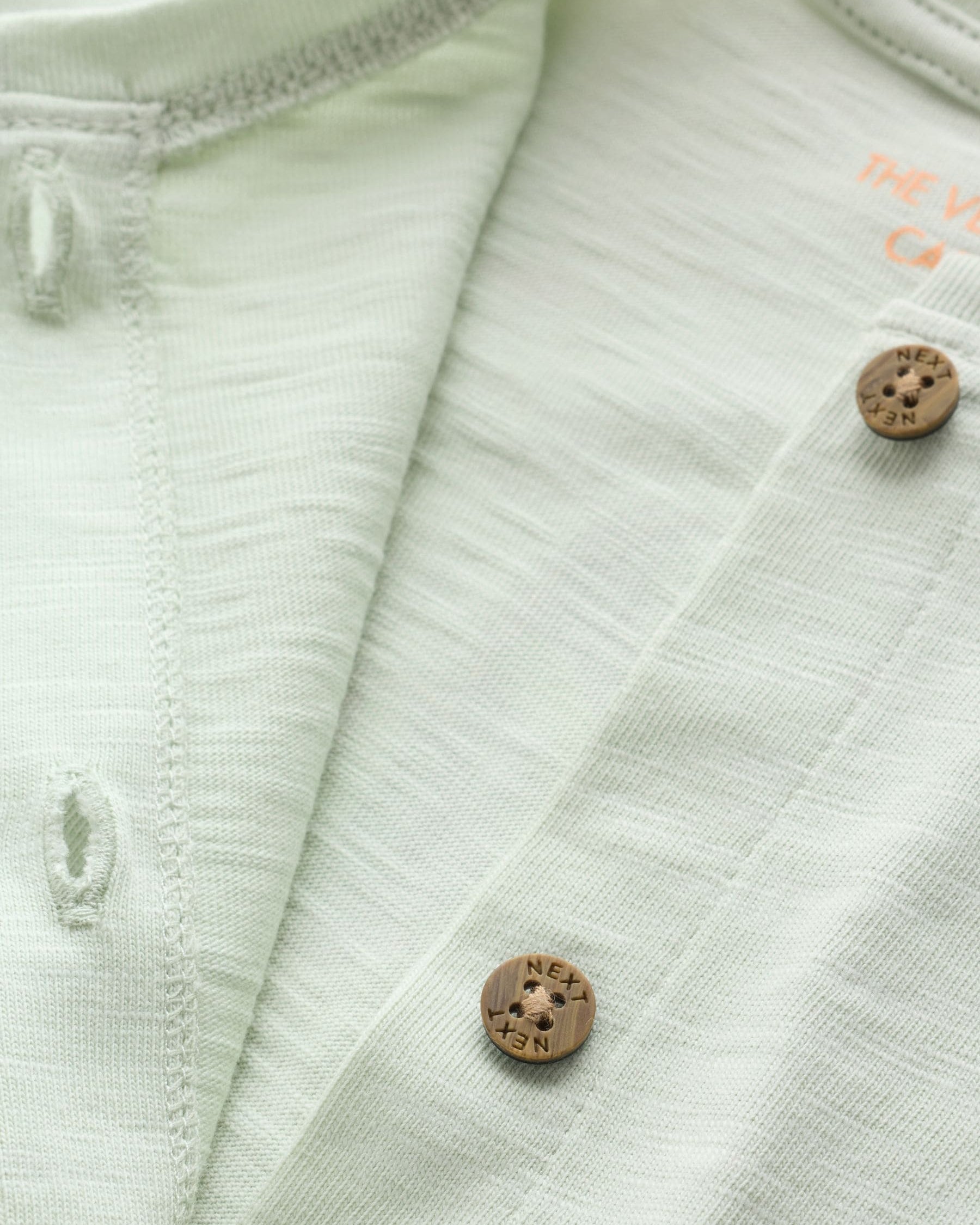 Close-up of wooden buttons on front placket of mint green slub cotton baby romper