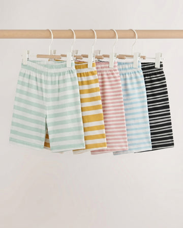Five kids' striped pull-on shorts fanned out flat lay — mint, mustard, pink, blue, and black stripe patterns with elastic waistband, on light grey background.