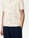 boy wearing a textured cream shirt with button details and navy pants on a white background