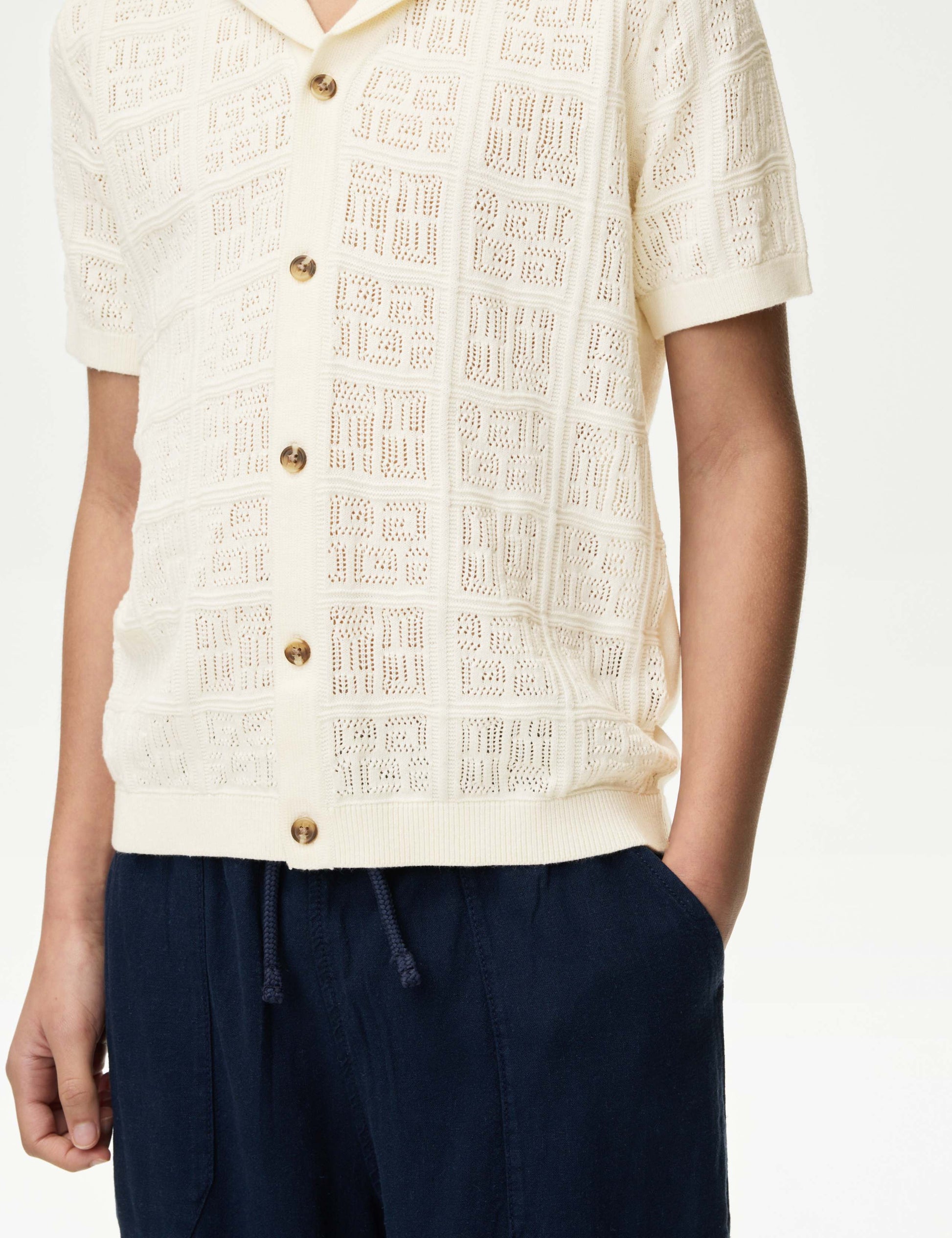 boy wearing a textured cream shirt with button details and navy pants on a white background