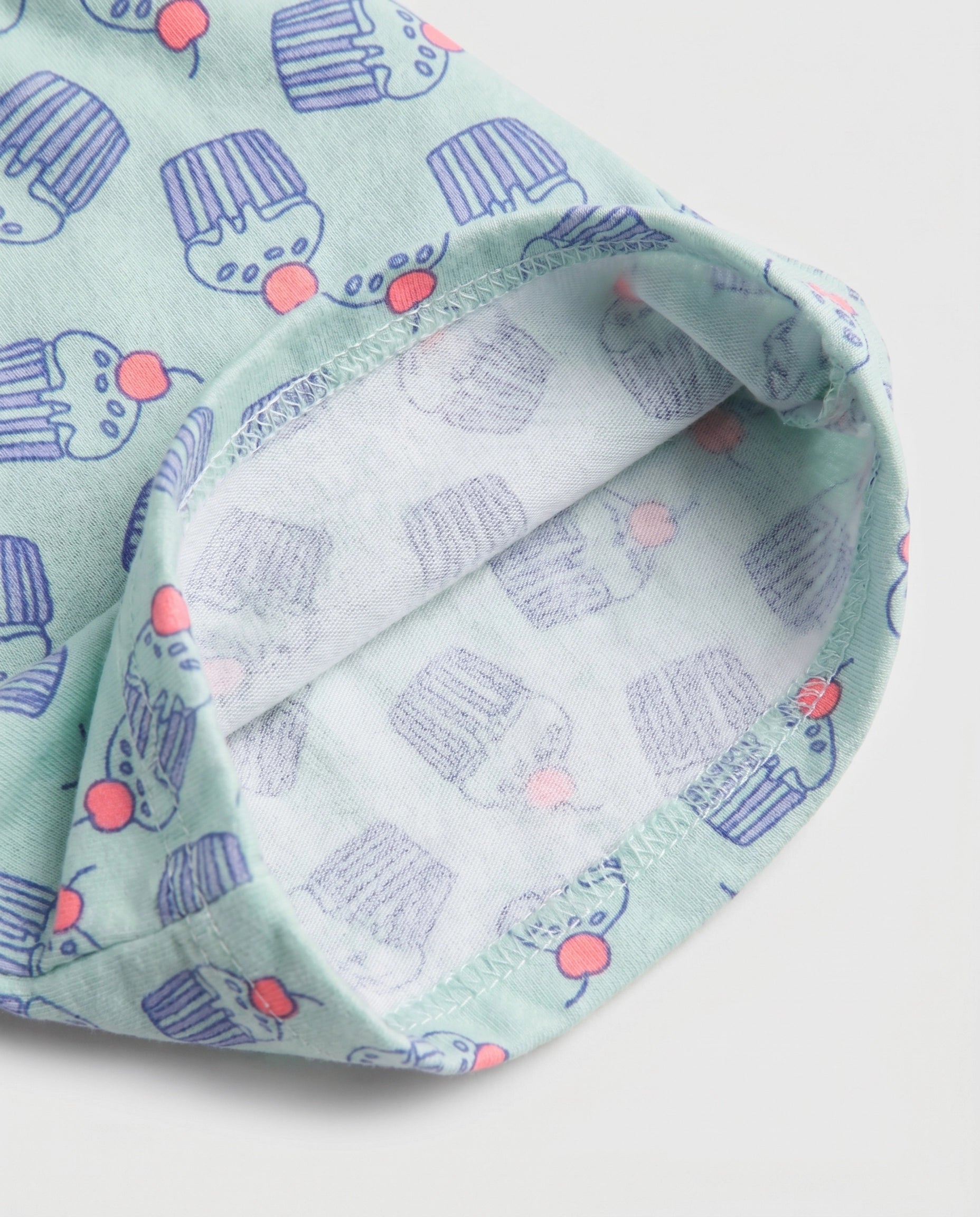 Close-up of mint green cupcake print cotton fabric showing matching printed soft inner lining and overlock stitch hem detail of girl's short pant