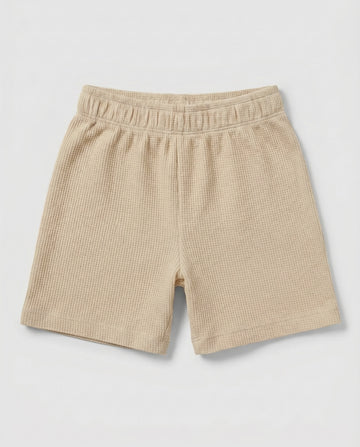 Full front flat-lay view of toddler waffle cotton short pants in warm beige with elasticated waistband and relaxed short-length silhouette on a light grey background.