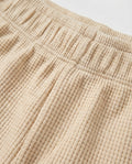 
Close-up of toddler waffle-knit cotton short pants in warm beige showing elasticated waistband construction and detailed grid-textured fabric surface.