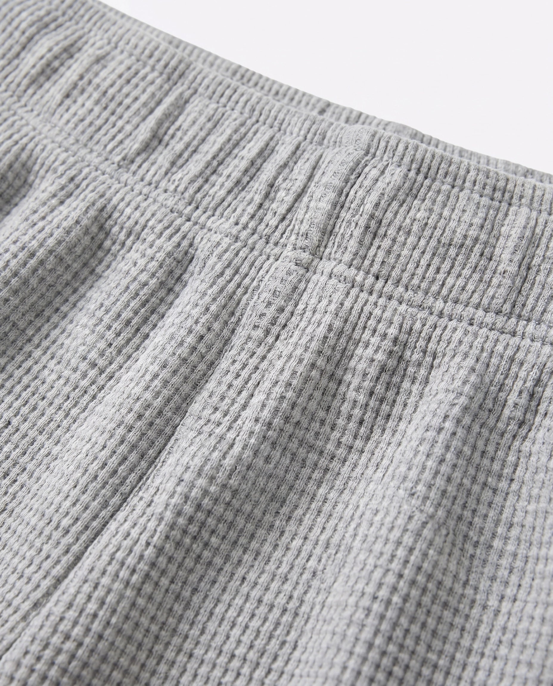 Close-up of toddler waffle-knit cotton short pants in light grey showing elasticated waistband detail and distinctive grid-textured fabric surface.