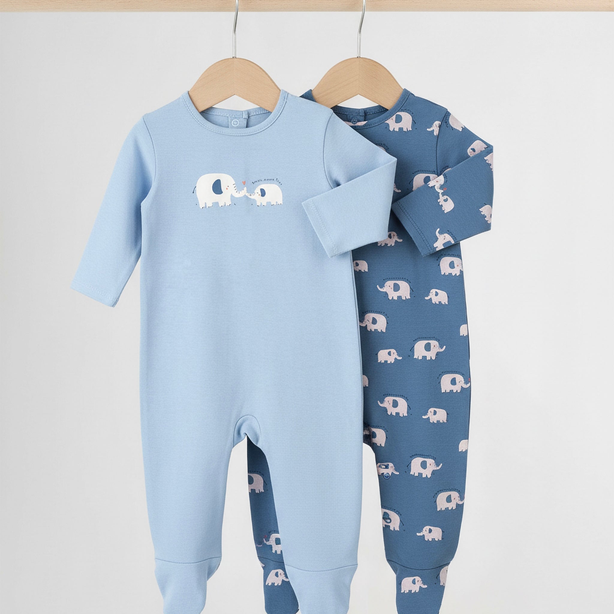 Two baby onesies with elephant patterns on hangers against a white background