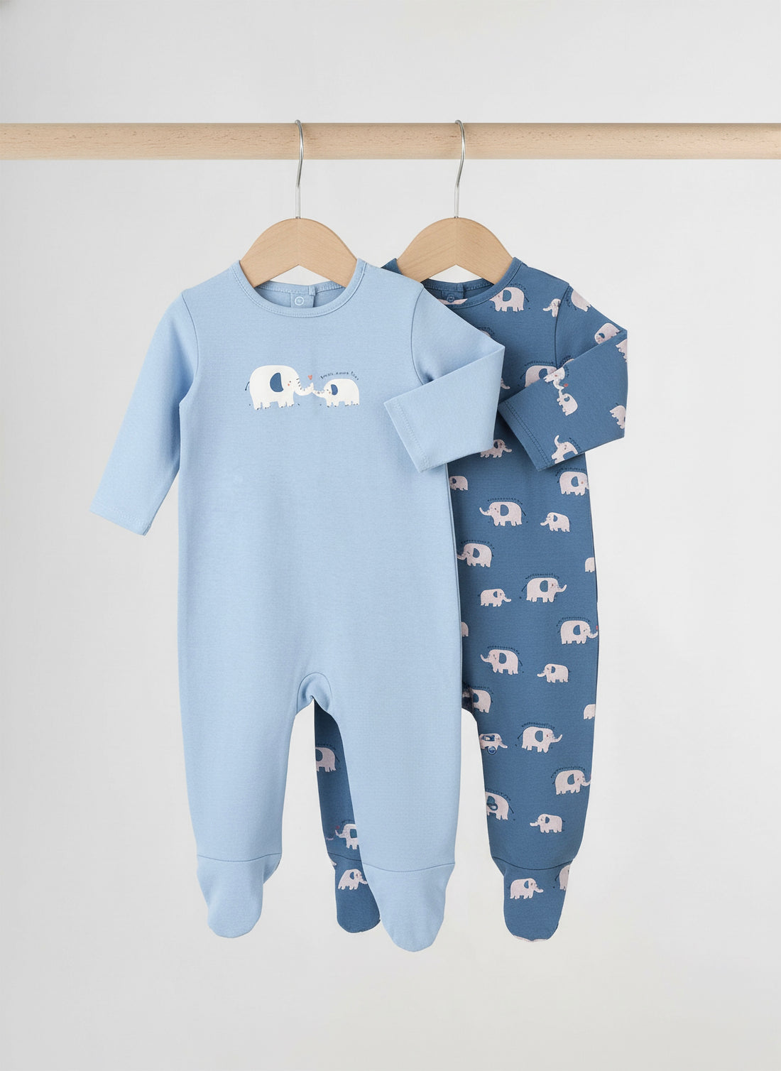 Two baby onesies with elephant patterns on hangers against a white background