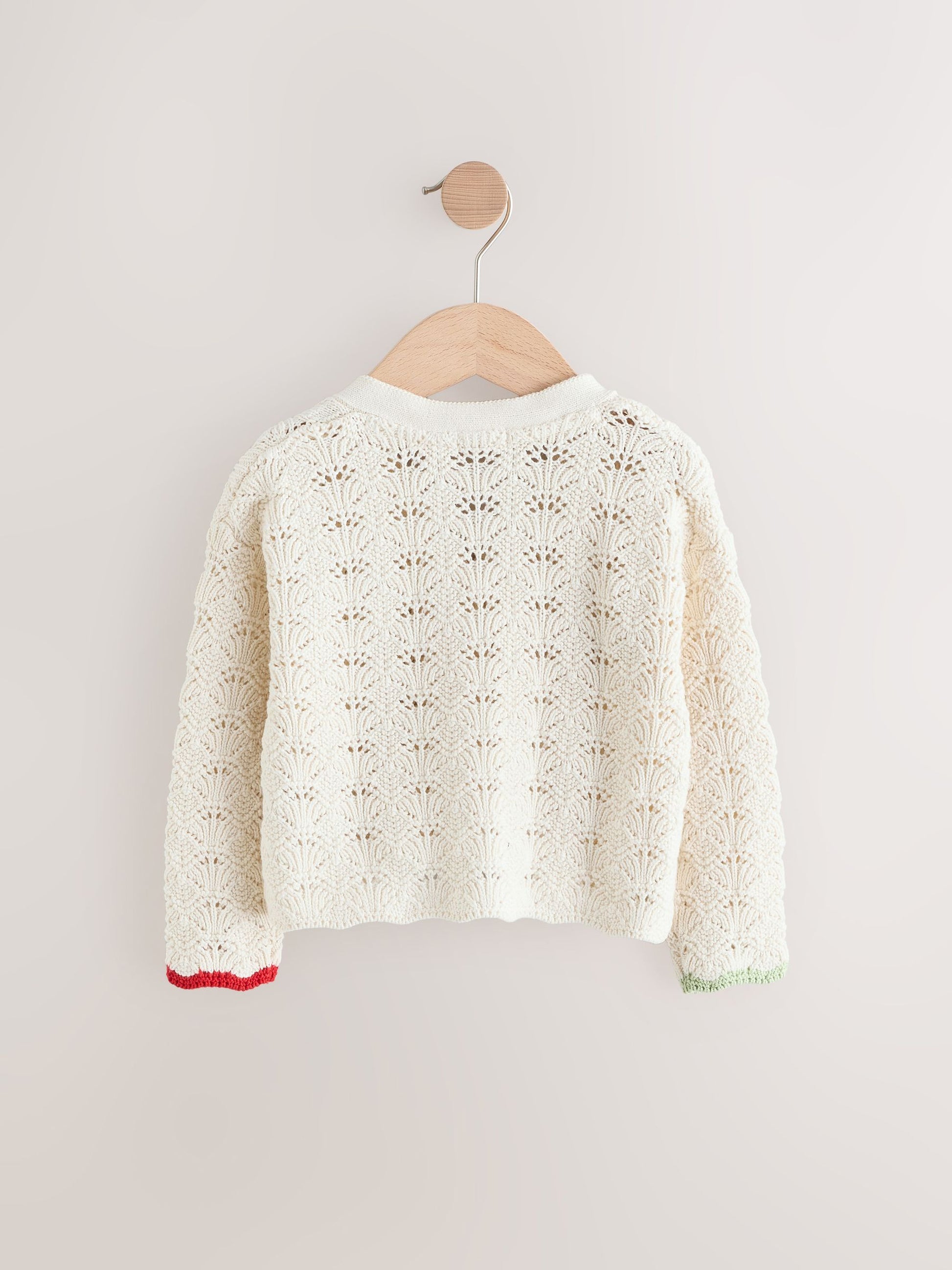 White lace cardigan on a wooden hanger against a light gray background