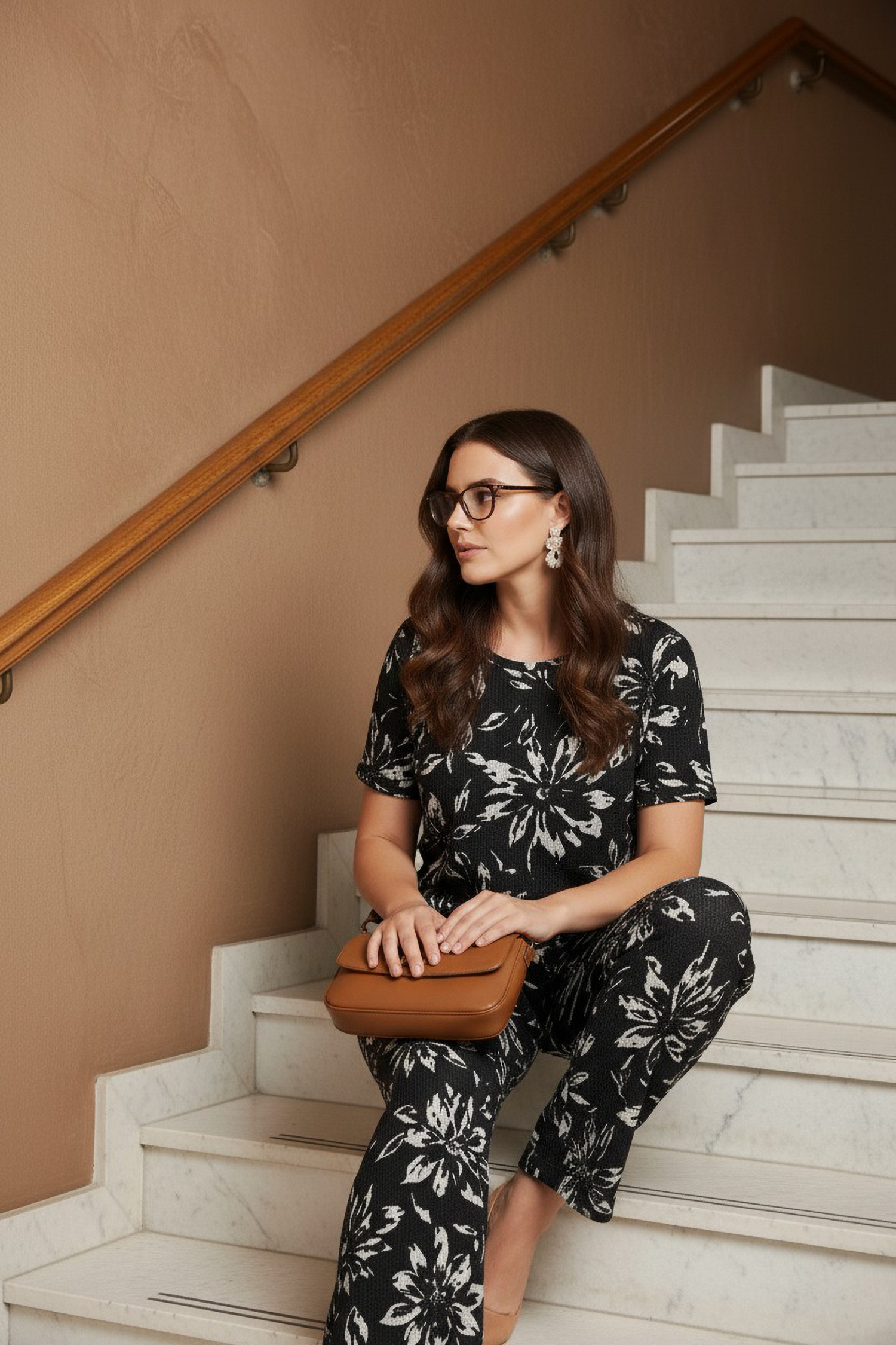 Woman in a black floral outfit sitting on a staircase holding a brown clutch.