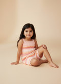 Young girl sitting wearing a striped Jumpsuit against a beige background