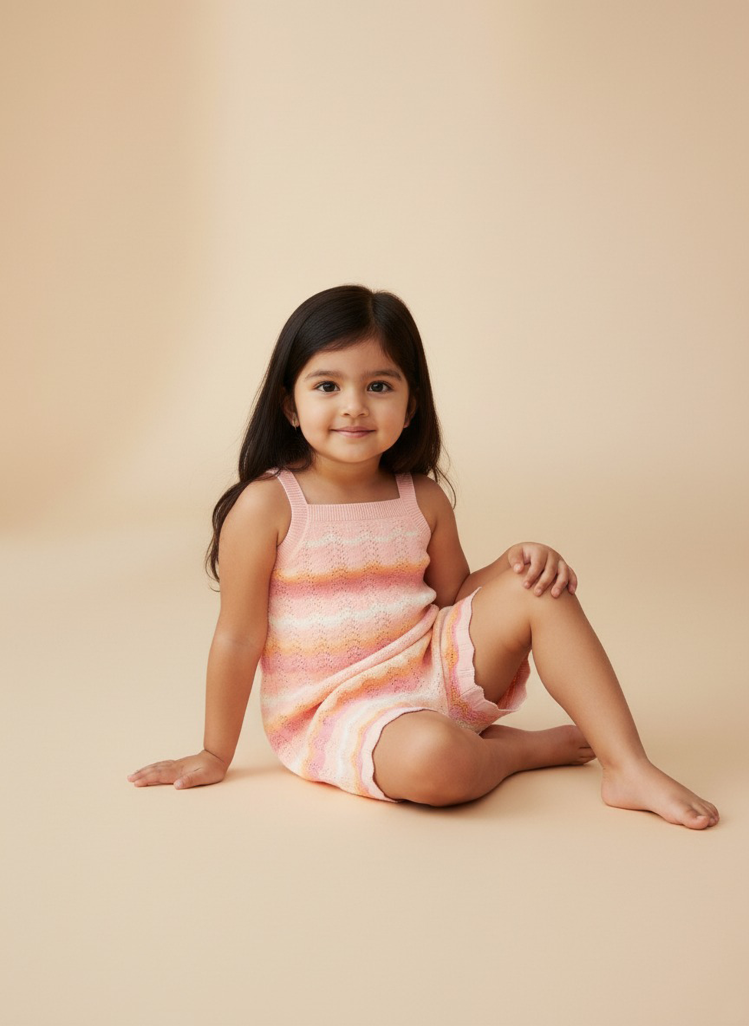 Young girl sitting wearing a striped Jumpsuit against a beige background