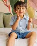 Boy sitting on a bed wearing a PTex Fashion sky blue carrot print cotton shirt with navy shorts