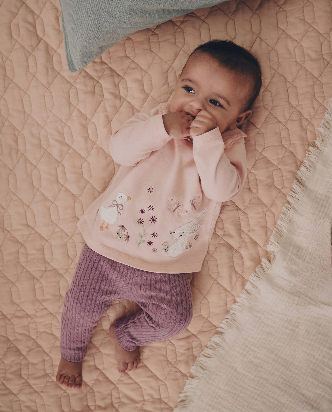 Baby girls' cable-knit leggings 3-pack in cream, blush pink, and mauve purple, flat lay on grey background