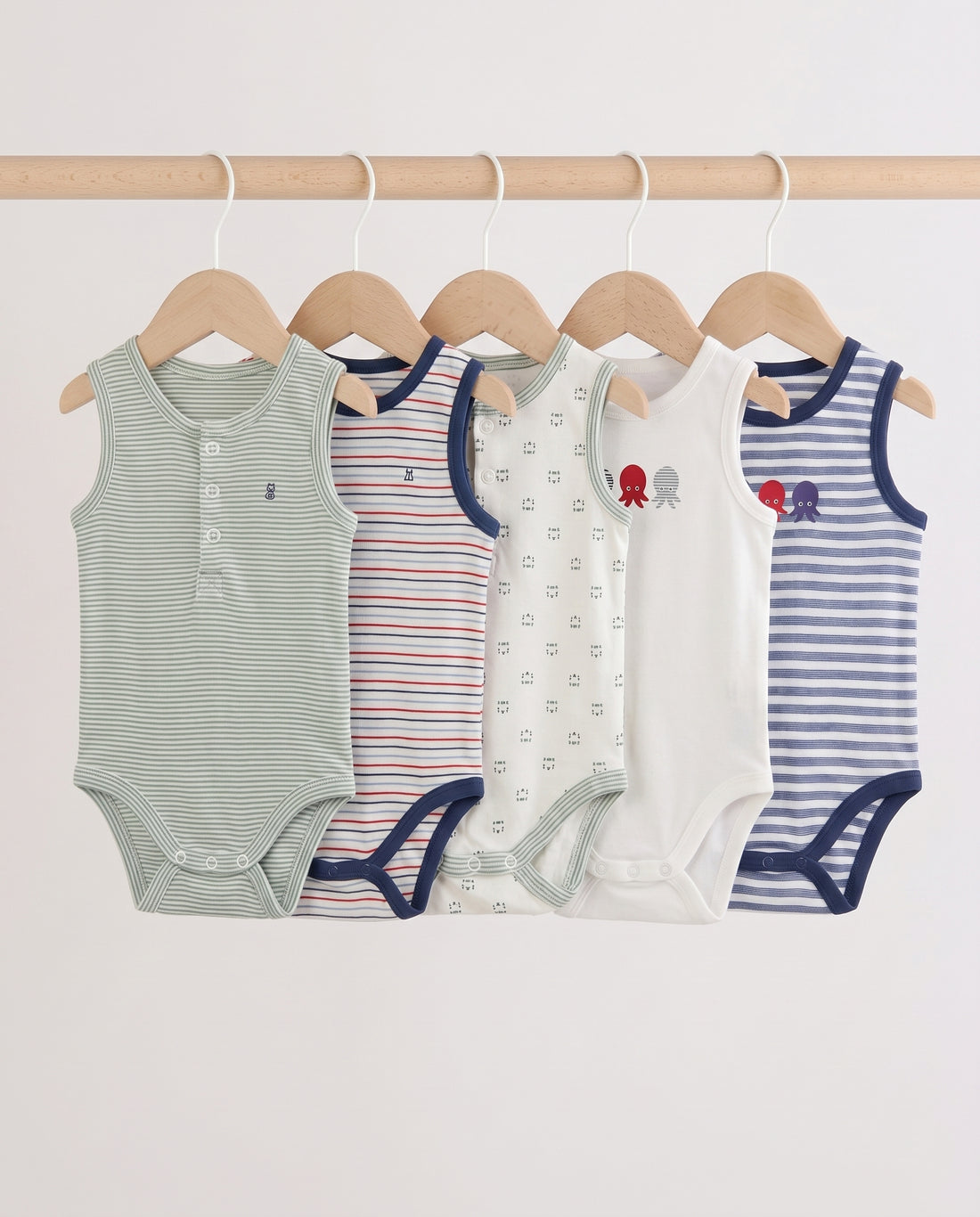 Five baby sleeveless bodysuits in mixed stripe and print designs hanging on wooden hangers — sage stripe, red multi-stripe, cream print, white octopus graphic, and blue stripe