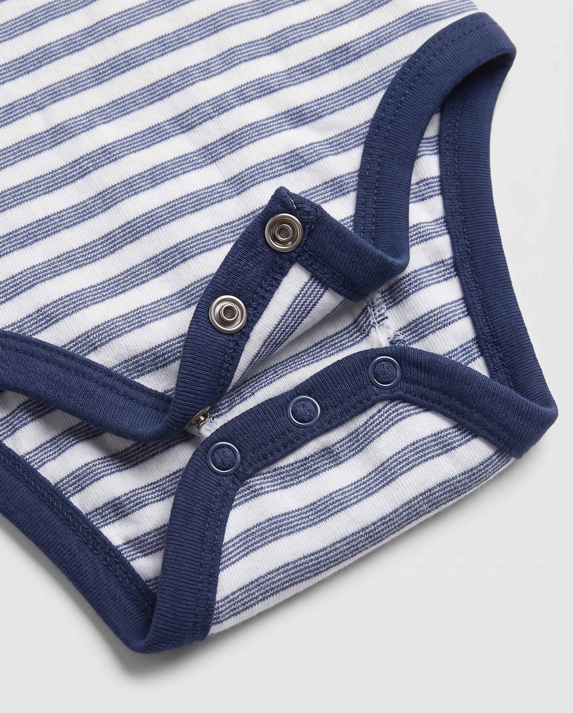 Close-up of baby bodysuit crotch snap fasteners on blue and white striped cotton fabric with navy ribbed trim