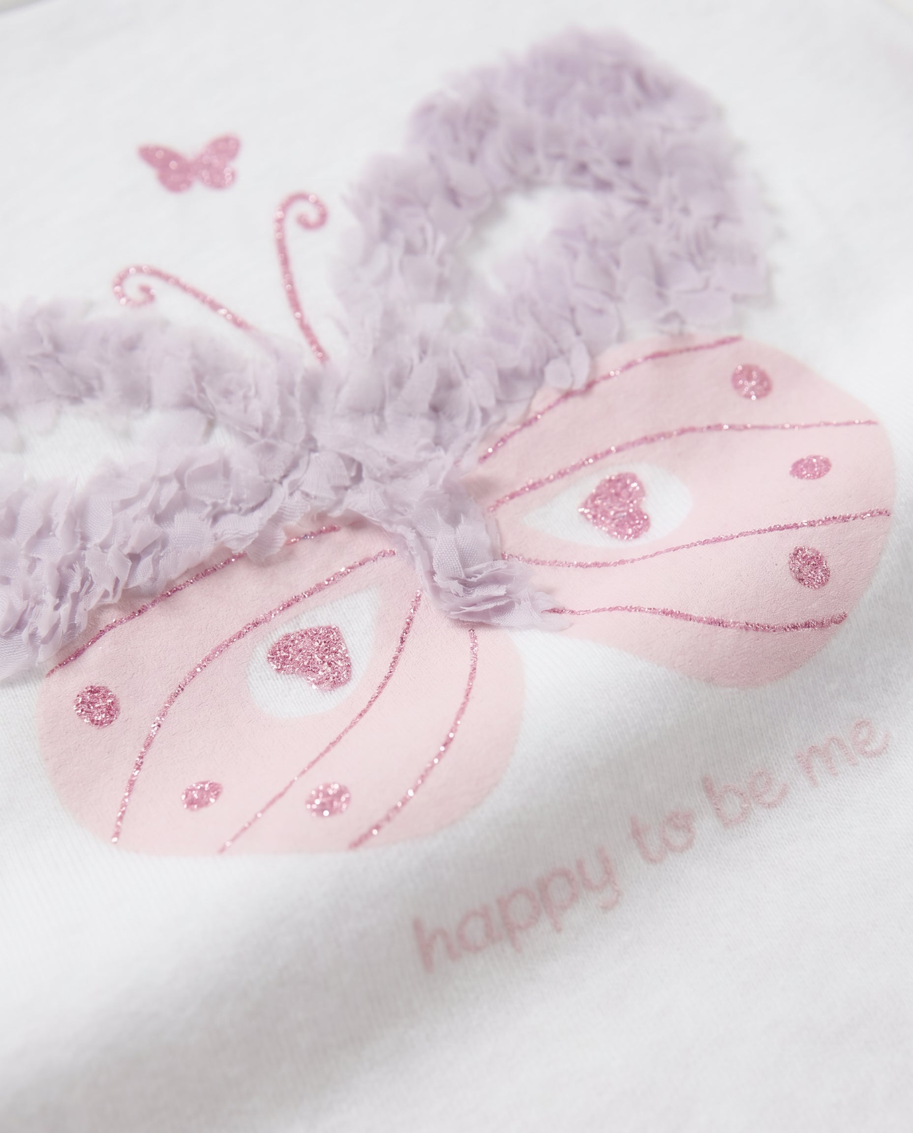 Close-up of pink glitter butterfly with raised ruffle wings and happy to be me text on white tee