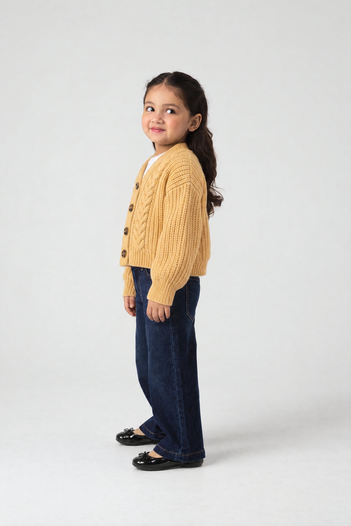Girl wearing PTex Fashion mustard yellow chenille boxy cardigan over a white tee with dark wide-leg jeans, side view