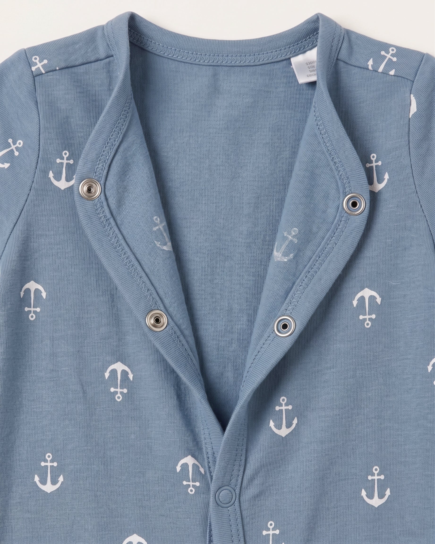 Close-up of steel blue baby jumpsuit neckline showing white anchor print pattern and silver snap button detail
