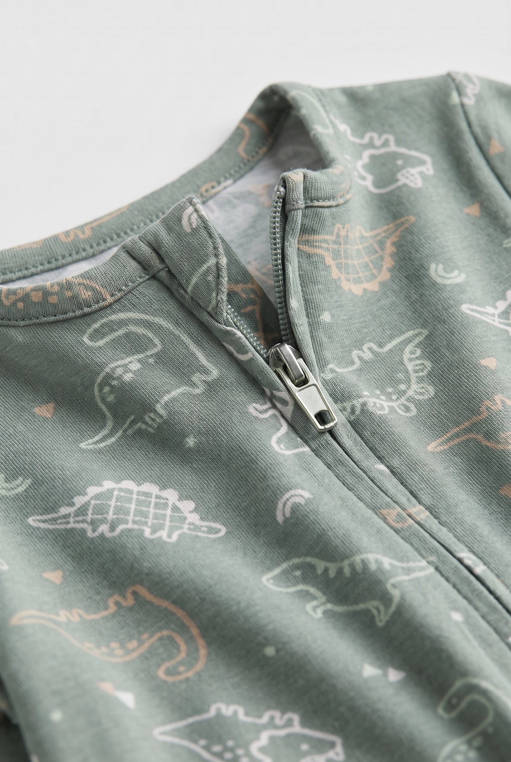 Close-up of sage green baby romper showing dinosaur print and two-way zipper detail