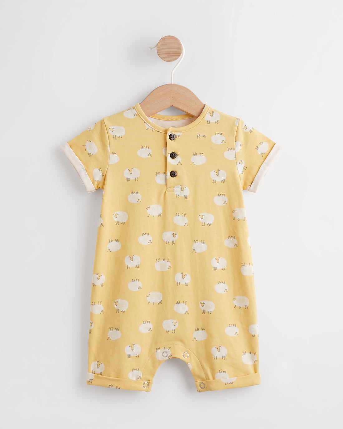 Yellow sheep print baby romper on a wooden hanger showing button placket and leg press studs — PTex Fashion