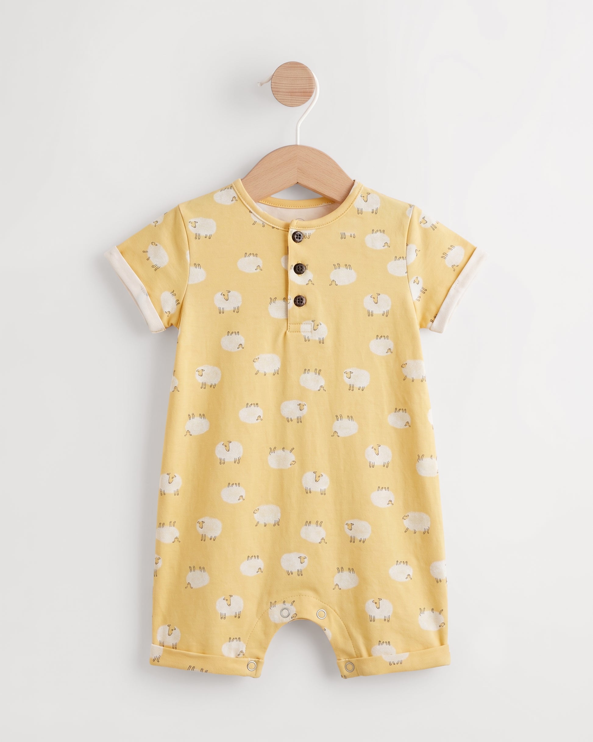 Yellow sheep print baby romper on a wooden hanger showing button placket and leg press studs — PTex Fashion