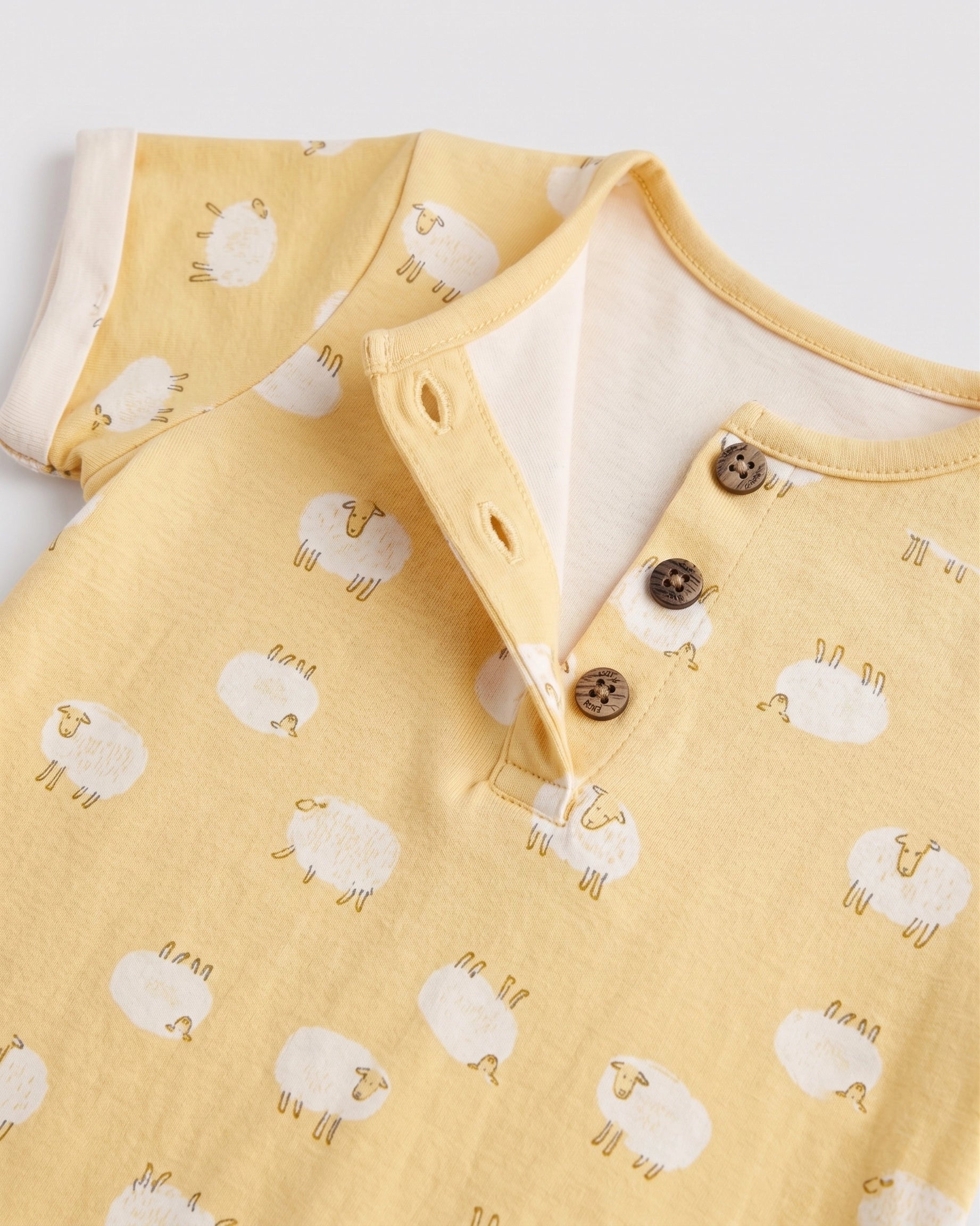 Close-up of yellow sheep print baby romper showing coconut buttons and cream placket lining — PTex Fashion