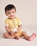 Baby sitting in yellow sheep print short cotton romper holding a crochet toy — PTex Fashion