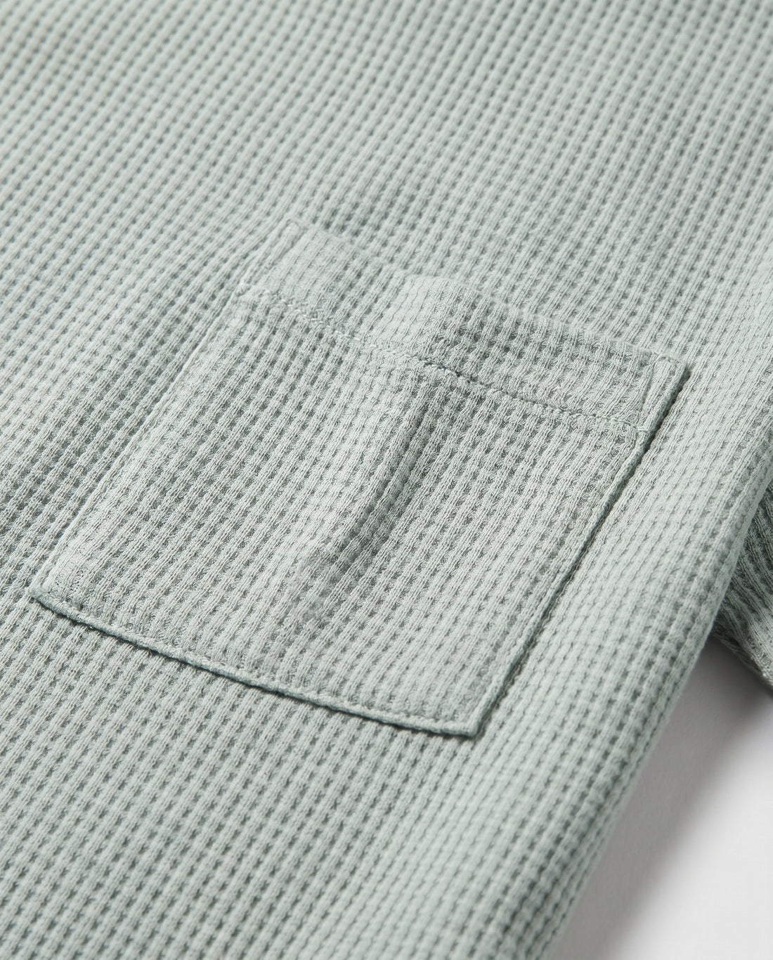 Boy's sage mint waffle cotton t-shirt with relaxed boxy fit, ribbed crewneck, and patch chest pocket, photographed flat on a soft grey backdrop.