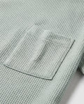 Close-up detail of waffle-knit texture and topstitched patch pocket on a sage mint boy's cotton t-shirt, showcasing fabric weave and stitching quality.