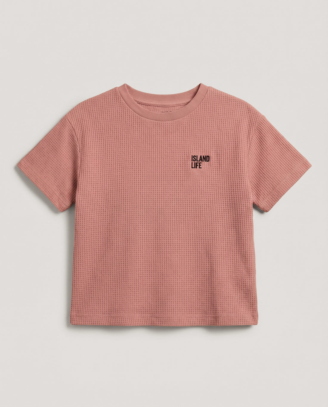 Boy's rusty rose waffle cotton t-shirt with "Island Life" black embroidery on the chest, relaxed boxy fit and ribbed crewneck, photographed flat on a soft grey backdrop.