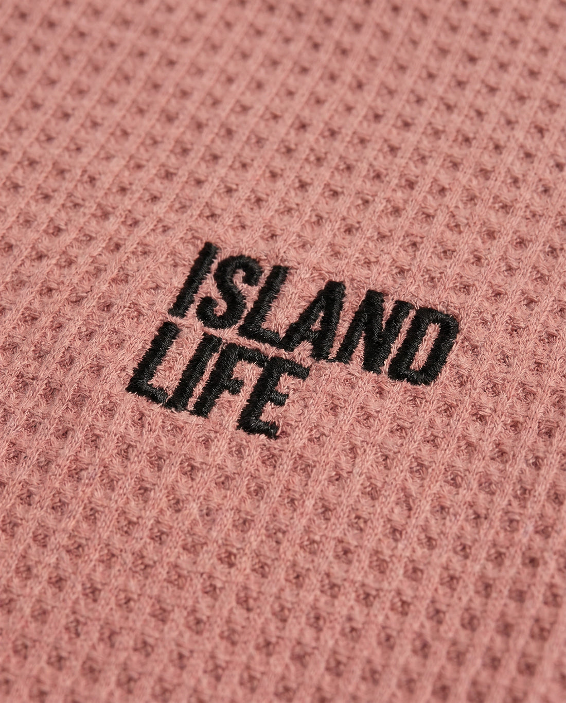 Boy's rusty rose waffle cotton t-shirt with "Island Life" black embroidery on the chest, relaxed boxy fit and ribbed crewneck, photographed flat on a soft grey backdrop.