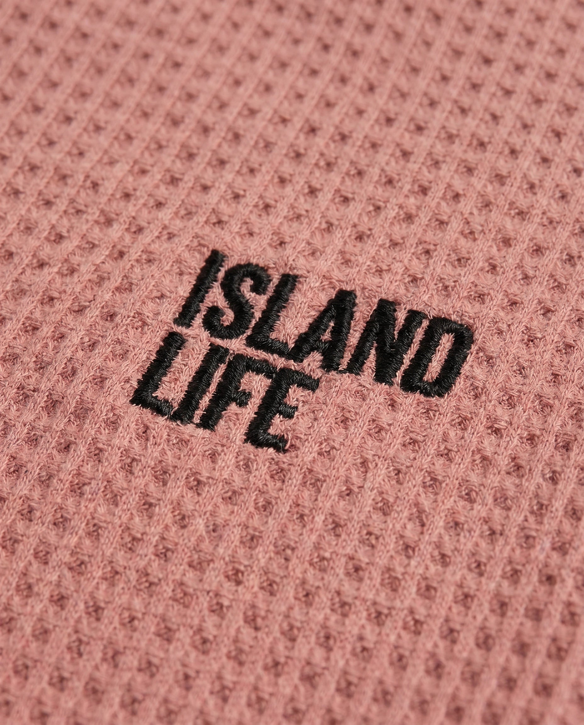Close look image of Boy's rusty rose waffle cotton t-shirt with "Island Life" black embroidery on the chest, relaxed boxy fit and ribbed crewneck, photographed flat on a soft grey backdrop.