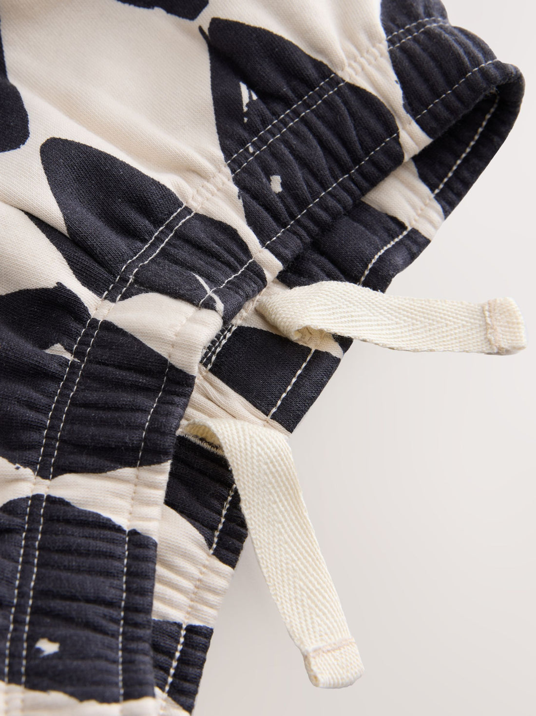PTex Fashion harlequin print kids' trousers in charcoal and off-white, shown on a wooden hanger