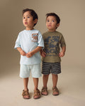 Two young boys wearing graphic t-shirts and stripe shorts on a beige background from PTex Fashion.